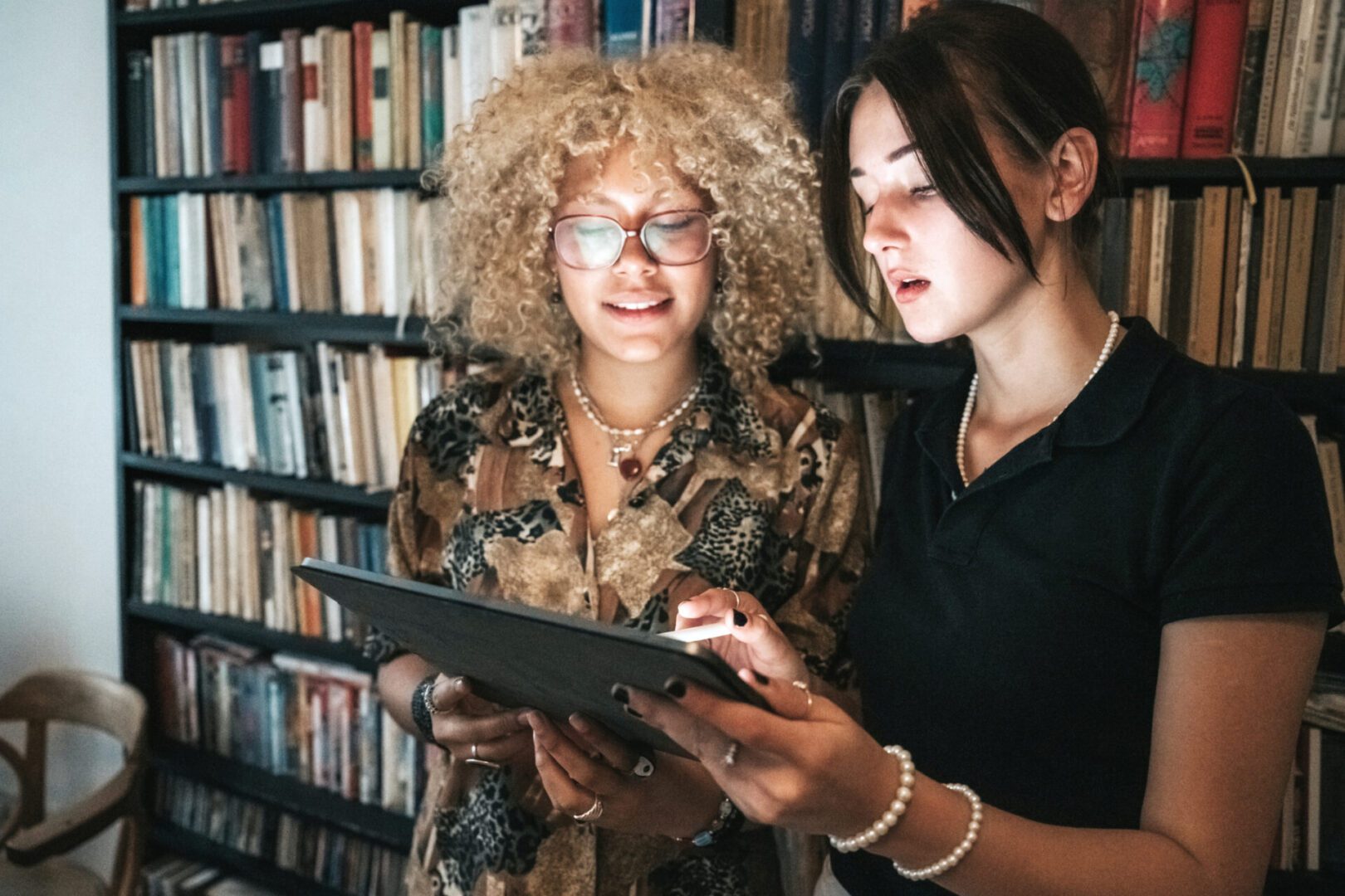 Two women using a tablet in library.