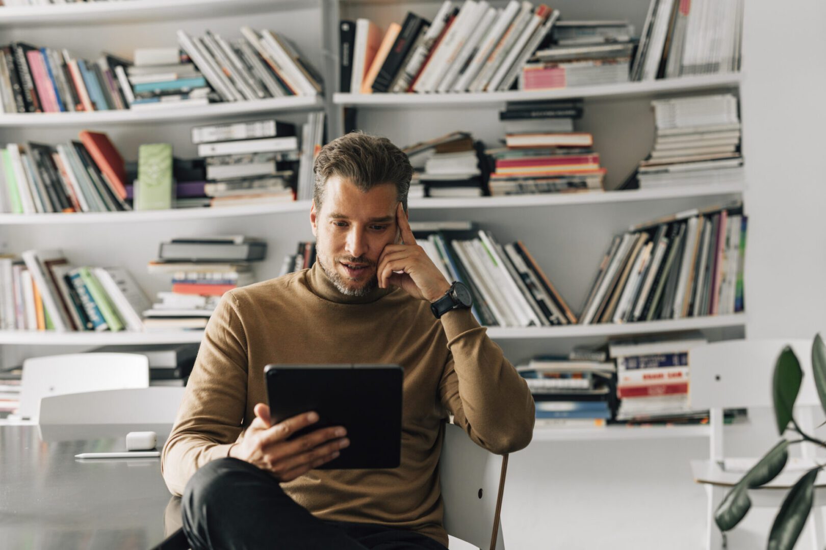 Man reading tablet in front of bookshelf