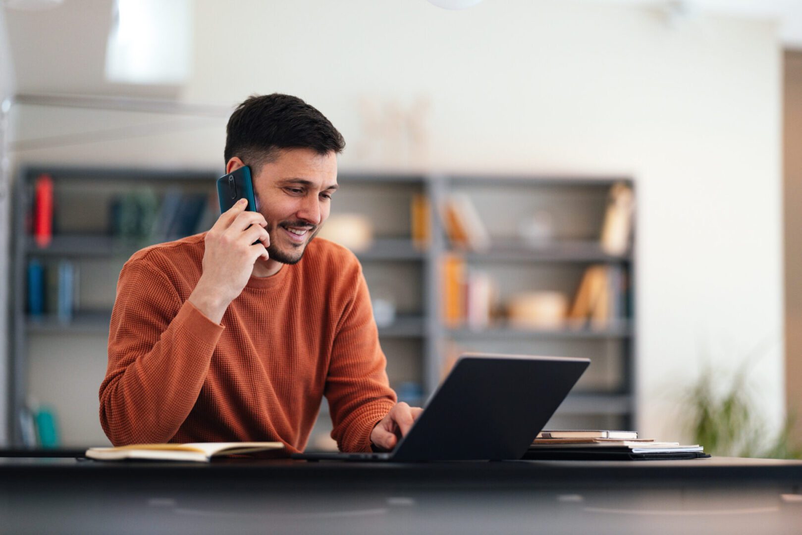 Smiling person multitasking with phone and computer